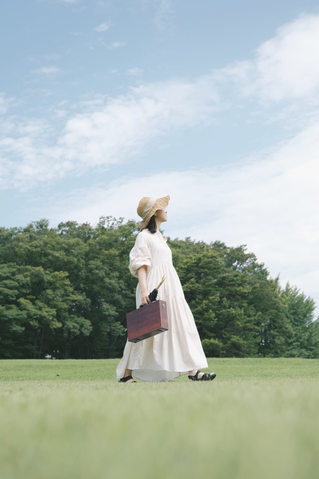 緑の公園を歩く白いワンピースの人物